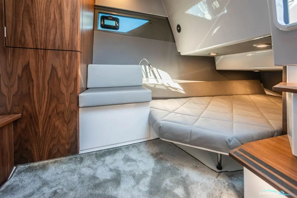 Interior of a modern boat cabin featuring a grey bed, seating area, wooden accents, and natural light from a window.